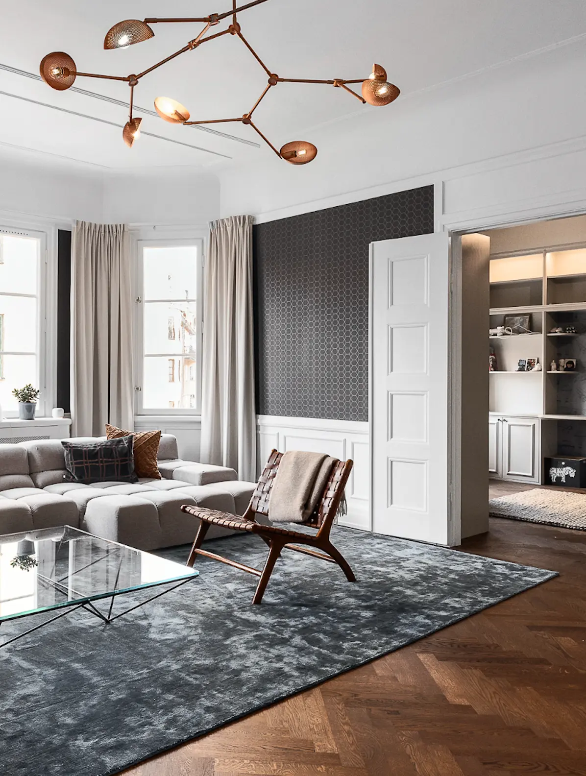 Elegant vardagsrum med grå soffa, designstol, glasbord och mässingslampa